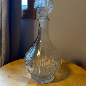 May include: A clear glass decanter with a textured, ribbed design. The decanter has a round, textured stopper.