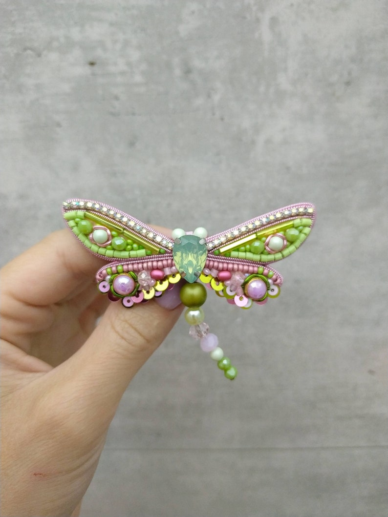 May include: A green and pink beaded dragonfly brooch with a clear crystal body. The wings are made of green and gold beads and sequins.