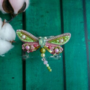 May include: A green and pink beaded dragonfly brooch with a crystal accent and a beaded tail.