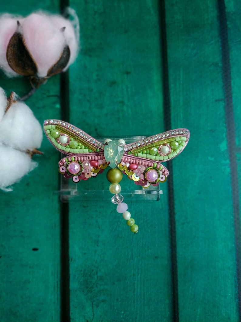 May include: A green and pink beaded dragonfly brooch with a crystal accent and a beaded tail.