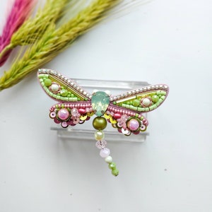 May include: A green and pink beaded dragonfly brooch with a clear crystal body and a beaded tail.