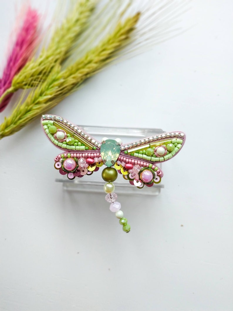 May include: A green and pink beaded dragonfly brooch with a clear crystal body and a beaded tail.