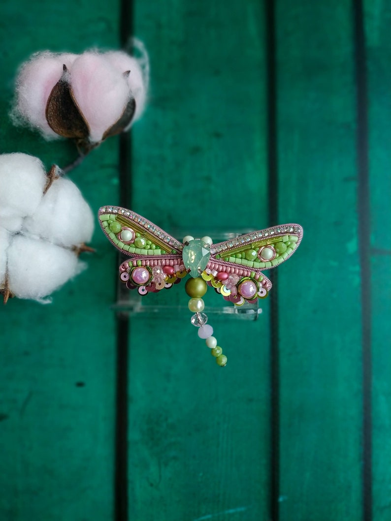 May include: A green and pink beaded dragonfly brooch with a clear crystal body and a beaded tail.