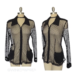 May include: Black fishnet jacket with a collared neckline, long sleeves, and two front pockets. The jacket has a zipper closure and is displayed on a mannequin. The bottom hem and cuffs have a scalloped edge.