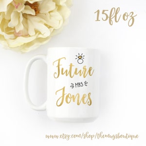 K&ouml;nnte beinhalten: Wei&szlig;e Keramiktasse mit goldener Aufschrift "Future Mrs. Jones" mit einer kleinen Ringzeichnung &uuml;ber dem Text. Die Tasse ist 15 fl oz.