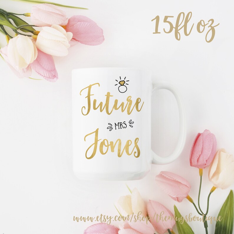 K&ouml;nnte beinhalten: Eine wei&szlig;e Keramiktasse mit einem goldenen Design, auf dem "Future Mrs. Jones" steht und eine kleine Zeichnung eines Rings. Die Tasse hat ein Fassungsverm&ouml;gen von 15 fl oz.