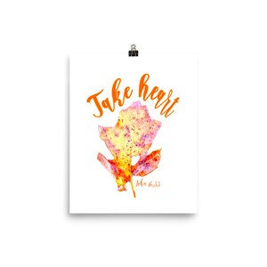 May include: A white printable art print with the text "Take heart" in orange lettering. A watercolour painting of a yellow, orange, and pink leaf is in the centre of the print. The text "John 16:33" is below the leaf.