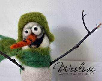 Könnte beinhalten: Ein grüner Filz-Schneemann mit einer Karottennase und Kulleraugen, der einen grünen Filzhut und einen Schal trägt. Der Schneemann hält zwei Äste in seinen Armen.