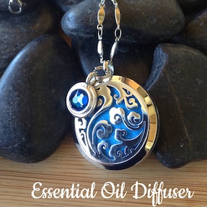 May include: Silver essential oil diffuser pendant with a blue gemstone and a decorative blue and silver design. The pendant hangs on a silver chain. The text "Essential Oil Diffuser" is at the bottom of the image.