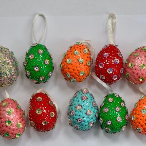 May include: Ten colorful Easter eggs decorated with sequins. The eggs are in various colors, including red, green, blue, pink, and orange. Each egg has a white string attached to the top for hanging.