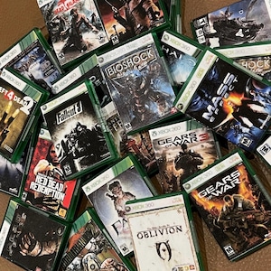 May include: A collection of Xbox 360 video game cases, including titles like Fallout 3, Gears of War, Red Dead Redemption, and Oblivion. The cases are green and feature various game characters and logos.