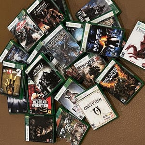 Puede incluir: Una colecci&oacute;n de cajas de juegos de Xbox 360, que incluyen t&iacute;tulos como Fallout 3, Left 4 Dead, Red Dead Redemption, Gears of War y Oblivion. Las cajas son verdes y negras con varios personajes y logotipos de juegos.