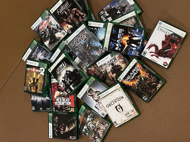 Puede incluir: Una colecci&oacute;n de cajas de juegos de Xbox 360, que incluyen t&iacute;tulos como Fallout 3, Left 4 Dead, Red Dead Redemption, Gears of War y Oblivion. Las cajas son verdes y negras con varios personajes y logotipos de juegos.