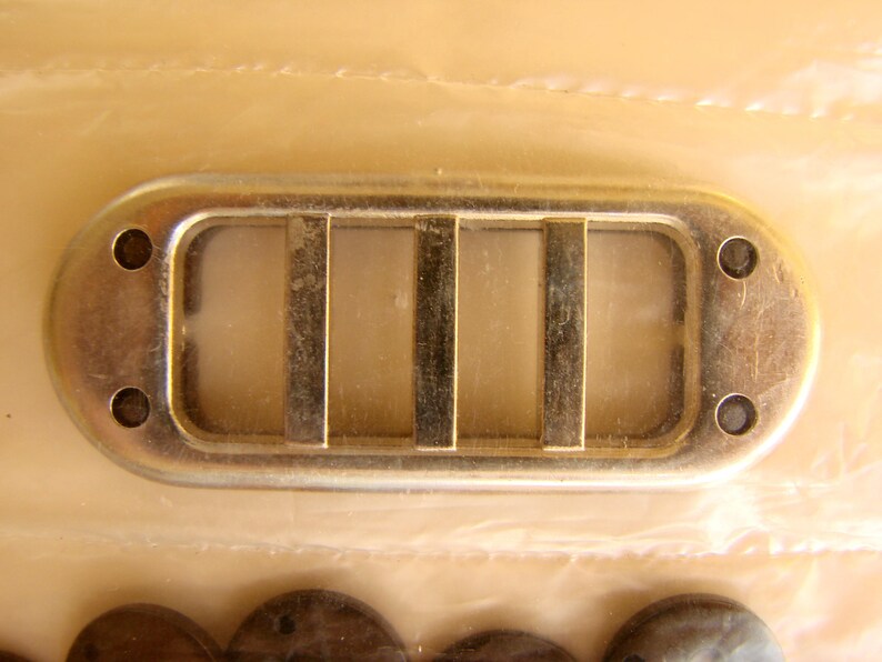 May include: A silver metal vent cover with four rectangular openings. The vent cover has a slightly rounded shape and is designed to be installed in a wall or ceiling.