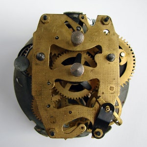 May include: Close-up of a gold-toned clock mechanism with intricate gears and levers. The mechanism is exposed, revealing the inner workings of the clock.
