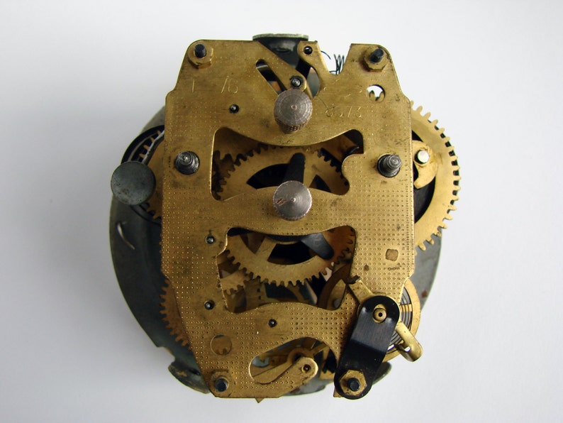 May include: Close-up of a gold-toned clock mechanism with intricate gears and levers. The mechanism is exposed, revealing the inner workings of the clock.