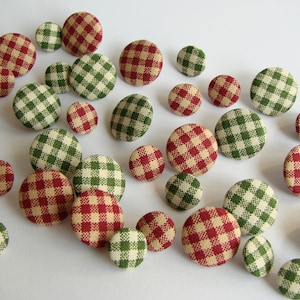 May include: Assortment of red and green gingham fabric buttons. The buttons are round and have a white background with red and green squares.