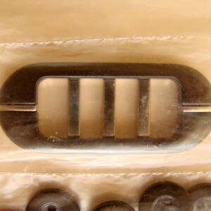 May include: A black plastic vent cover with four rectangular openings. The vent cover has a silver trim around the edges.