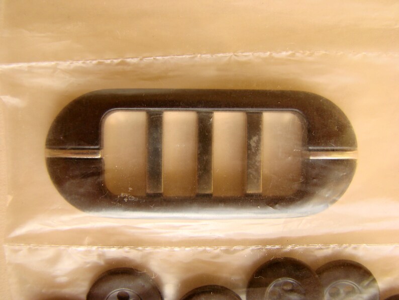 May include: A black plastic vent cover with four rectangular openings. The vent cover has a silver trim around the edges.