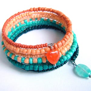 Puede incluir: Pulsera de cuentas multicolores con un dije en forma de corazón. La pulsera está hecha de cuentas turquesa, melocotón y naranja.