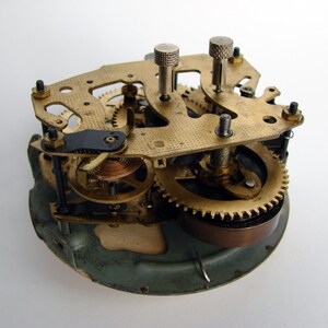 May include: Close-up of a vintage clock mechanism with brass gears and a copper spring. The clock face is missing, revealing the intricate inner workings.