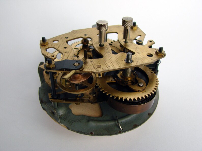 May include: Close-up of a vintage clock mechanism with brass gears and a copper spring. The clock face is missing, revealing the intricate inner workings.