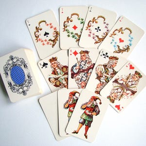 Op de afbeelding: Een kaartspel met sierlijke, bloemrijk omlijste symbolen en historische figuren. De kaarten tonen koningen en jokers in gedetailleerde historische kleding, met een blauw ruitpatroon op de achterkant van het doosje.
