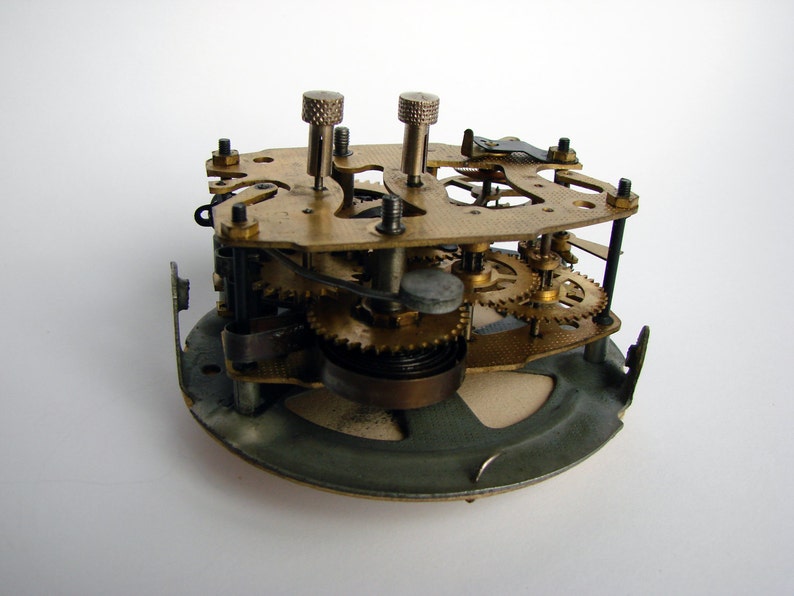 May include: Close-up of a clock mechanism with brass gears and a metal base. The clockwork is exposed, showing the intricate workings of the timepiece.