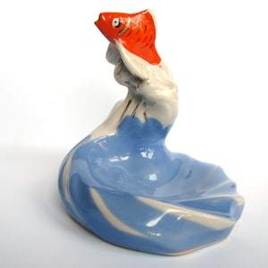 Peut inclure: Un plat à bijoux en céramique bleu et blanc avec une figurine de poisson rouge et blanc sur le dessus. Le plat est en forme de vague et le poisson saute hors de l'eau.