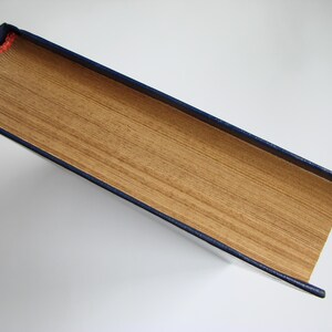 May include: A book with a blue cover and a gold spine. The book is closed and lying flat on a white surface.