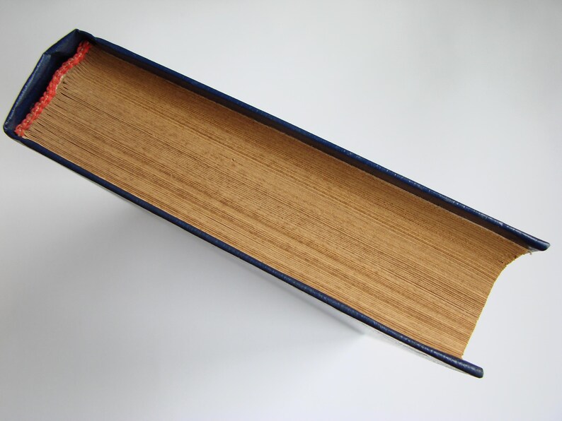 May include: A book with a blue cover and a gold spine. The book is closed and lying flat on a white surface.