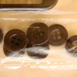 May include: A close-up of six black plastic buttons with four holes each. The buttons are arranged in a semi-circle on a clear plastic surface.