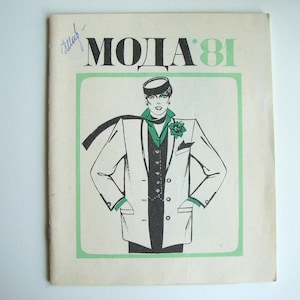 Op de afbeelding: Vintage mode tijdschriftomslag met de tekst "MODA 81" in zwart en groen. De illustratie toont een persoon in een wit pak met groene accenten, een zwarte sjaal en een hoed. Een blauwe handgeschreven notitie staat linksboven.