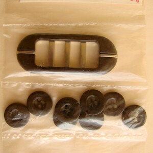 May include: A set of black buttons with a brown plastic buckle with a metal insert. The buckle has four slots.