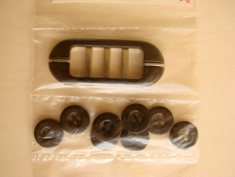 May include: A set of black buttons with a brown plastic buckle with a metal insert. The buckle has four slots.