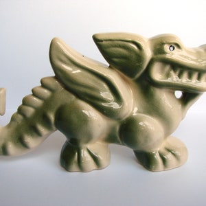 Op de afbeelding: Een keramiek drakenbeeldje met groene en witte glazuur. De draak heeft vleugels, een lange staart en een woeste uitdrukking.