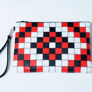 May include: A black, red, and white checkered clutch bag with a black strap.