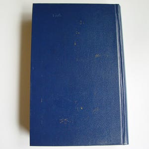 May include: A dark blue hardcover book with a smooth, textured cover. The book has a spine with gold lettering and a white label on the front cover.
