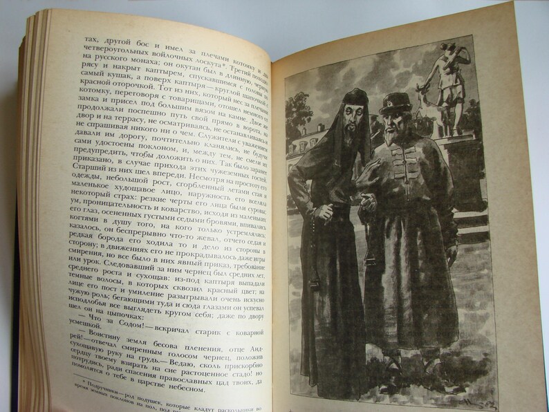 May include: Two men in long, dark robes stand together. The man on the left is wearing a black robe with a white collar and a long beard. The man on the right is wearing a dark brown robe with a white collar and a long beard. The man on the right has a white sash around his waist. The men are standing in front of a building with a white door.