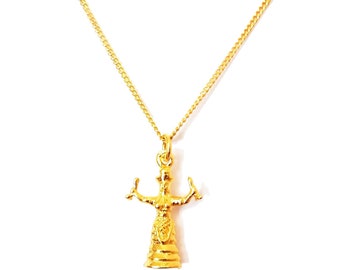 May include: A gold necklace with a pendant featuring a detailed figurine of a woman with outstretched arms. The pendant is a three-dimensional representation of a woman with a flowing gown and a crown.