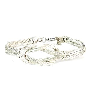 May include: A silver bracelet with a knotted design. The bracelet is made of twisted silver wire and has a clasp closure.