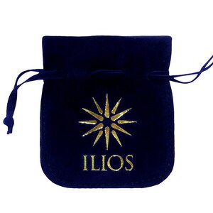 May include: A dark blue velvet pouch with a gold drawstring and a gold starburst logo with the word "ILIOS" printed below it.