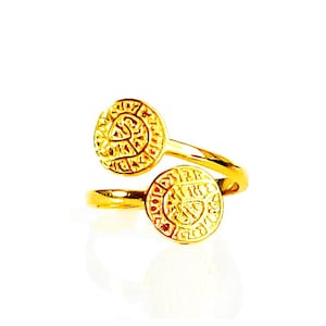 May include: A gold ring with two round, textured, coin-like elements. The ring is open and adjustable.