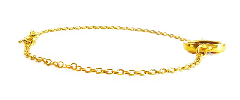 May include: A gold chain bracelet with a round, gold charm. The charm has a small, decorative detail on the side.