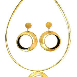 May include: A gold-toned jewelry set featuring a necklace and matching earrings. The necklace has a pendant with a circular design, and the earrings are large hoops. The set has a brushed metal finish with black accents.