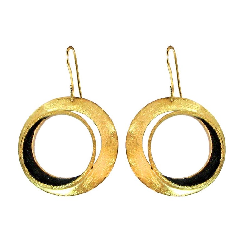 May include: A pair of gold-colored hoop earrings with a textured finish. Each earring features a large outer circle and a smaller inner circle, with a black accent on the inner circle. The earrings have a hook closure.