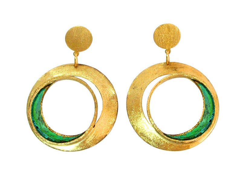 May include: A pair of gold-toned hoop earrings with a textured finish. Each earring features a large, open circle design with a smaller, curved inner shape, accented with green enamel. A small, round stud tops each earring.