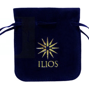 May include: A navy blue velvet drawstring pouch with a gold sunburst design and the word "ILIOS" printed below. The pouch has a soft texture and a drawstring closure.