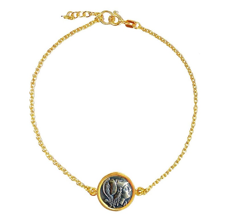 May include: A gold chain bracelet with a round pendant featuring a silver-toned image of a woman's profile. The pendant is surrounded by a gold rim.