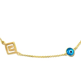 May include: A gold chain necklace with a blue evil eye charm and a gold pendant with a Greek key design.